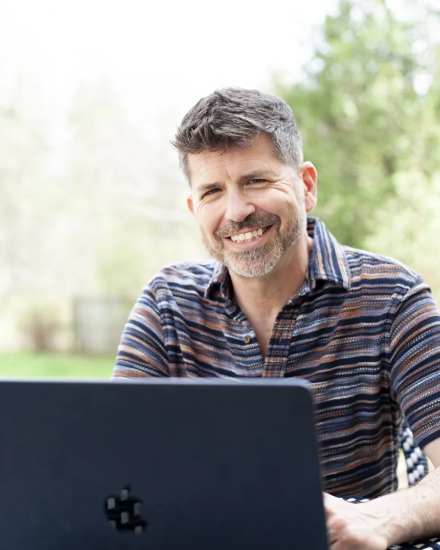 Jason smiling while seated at his laptop outdoors.