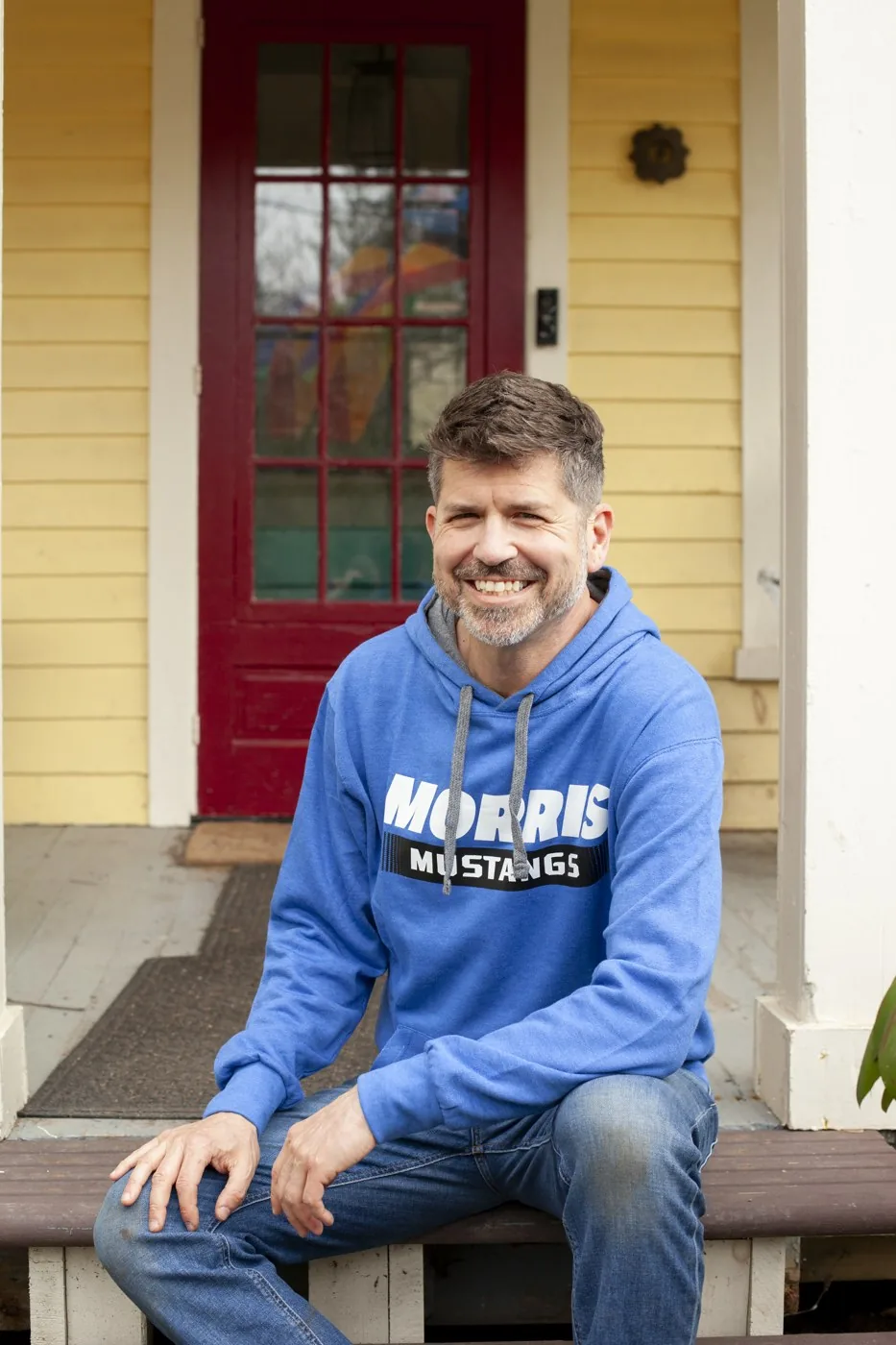Jason Cianciotto smiling on his porch in a blue Morris sweatshirt.